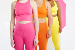 Tres mujeres vistiendo ropa deportiva de color rosa, naranja y amarillo